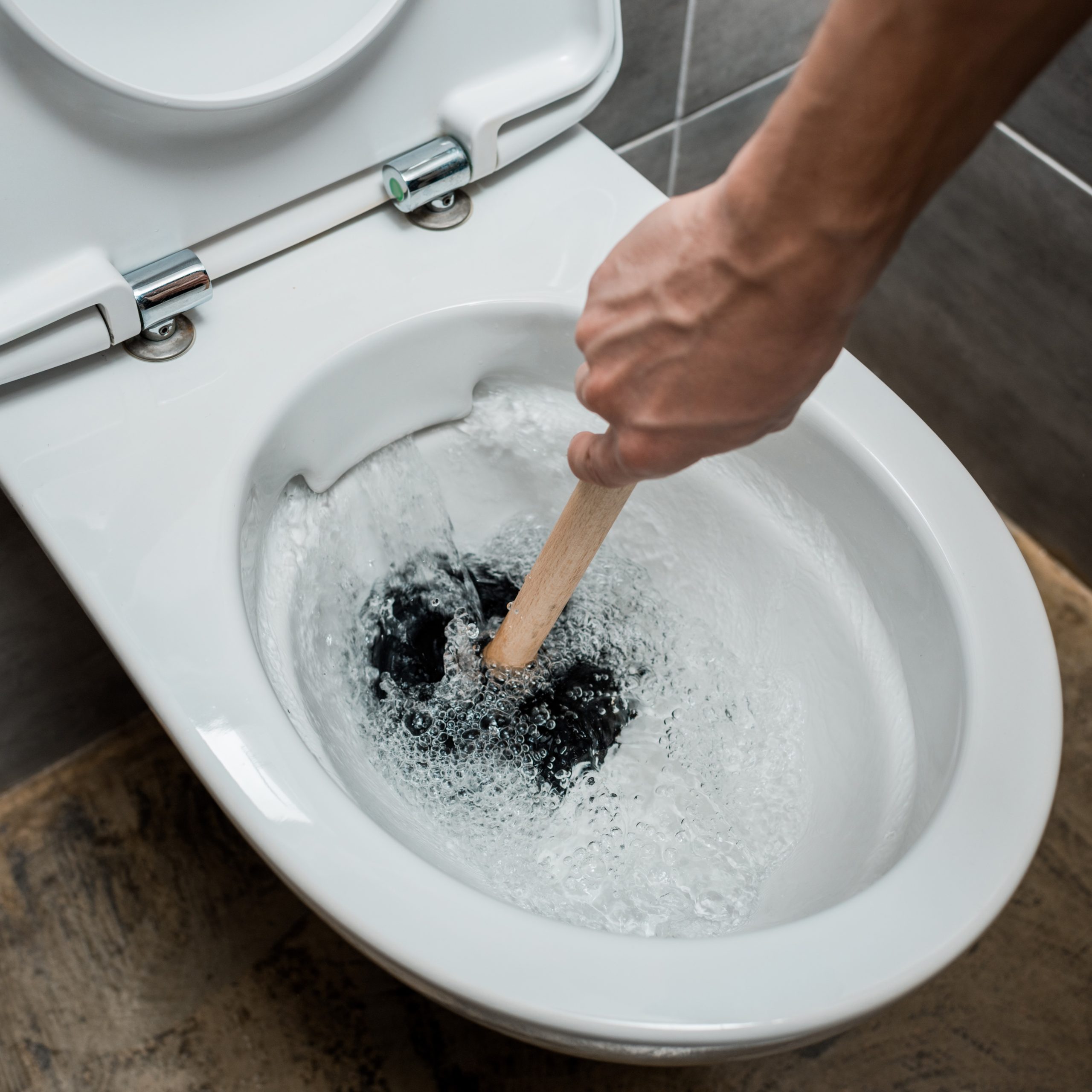 cropped view of plumber using plunger in toilet bowl during flushing in modern restroom with grey